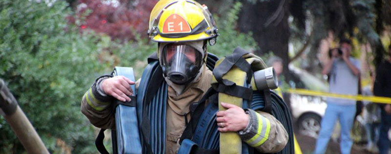 firefighter in full gear carrying hose.